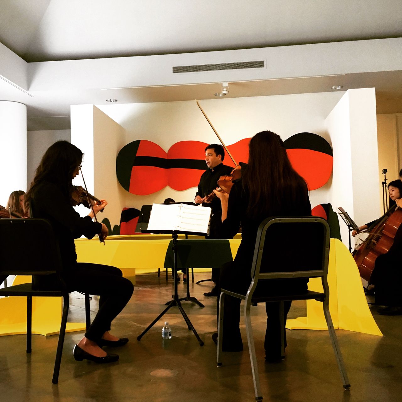 A photograph of a vocal tenor surrounded by string players and a colorful sculpture.