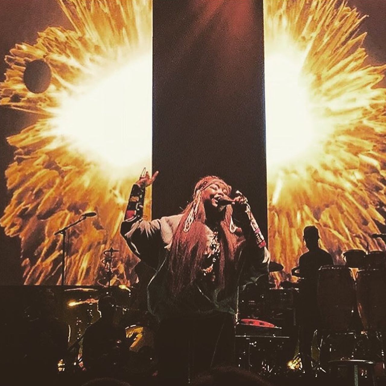 A woman on stage with two vertical screens behind her displaying a golden orange orb, spit down the middle as the screens are separated in space from one another.