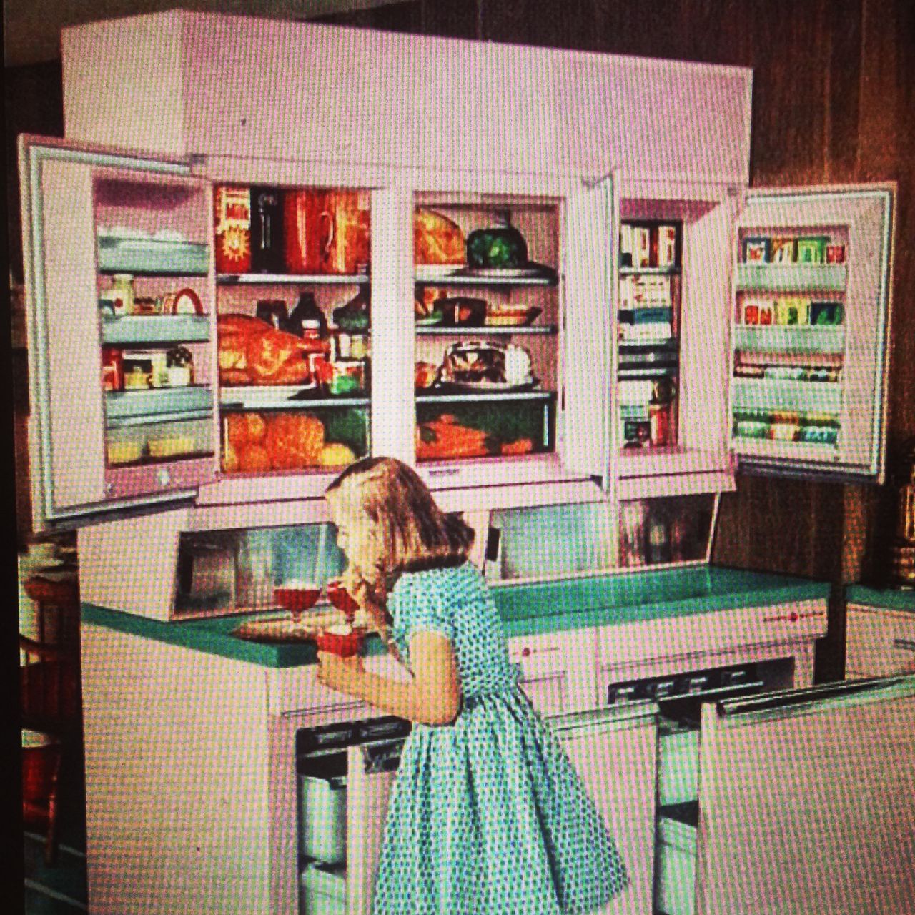 An image of a girl making drinks in a kitchen with a 1950s futuristic refrigerator with the doors open.