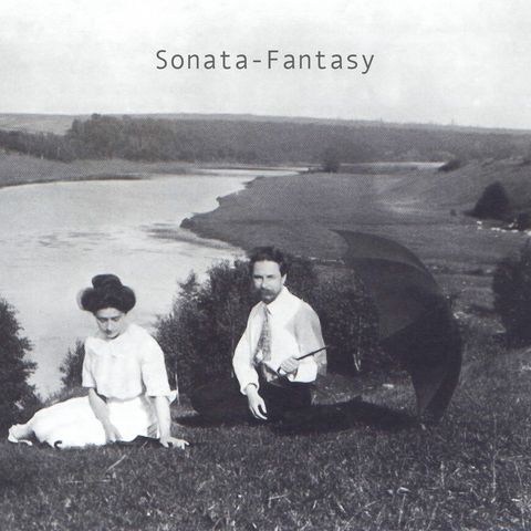 A monochromatic photograph of Alexander Scriabin and Tatiana Schloezer, seated on the grass with the Oka River in the background. Scriabin is holding an open umbrella in one hand.